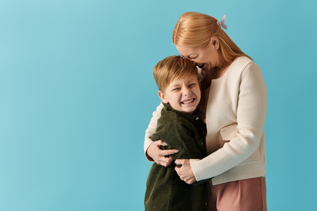 A mother leans down, sharing a warm embrace with her smiling son, creating a heartwarming bond.の写真素材