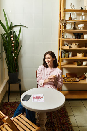 A pretty young woman smiles while sipping her drink at a modern cafe, surrounded by decor.のeditorial素材