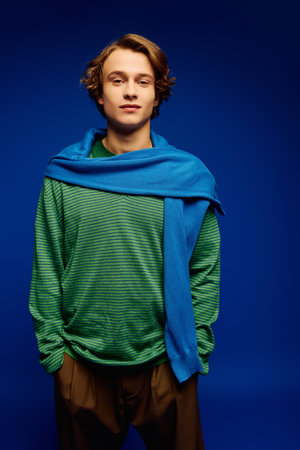 A stylish young man in modern attire confidently poses against a striking blue backdrop.のeditorial素材