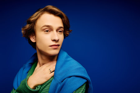 A young man showcases modern fashion with a confident pose against a vibrant blue background.のeditorial素材