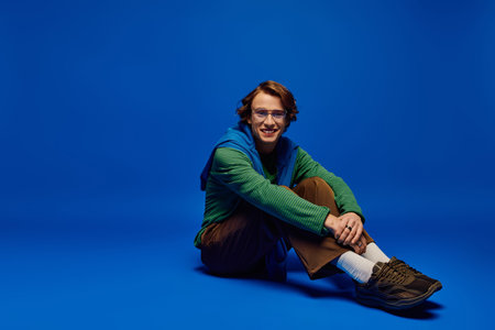 A young man in trendy clothes smiles warmly against a bright blue background.のeditorial素材