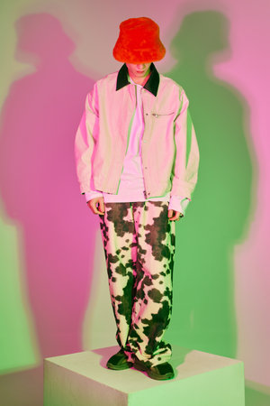 Confident young man on a pedestal flaunts bold fashion against vibrant backgrounds.