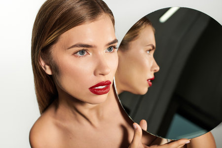 A young woman admires her reflection, exuding confidence and elegance in a stylish space.のeditorial素材