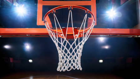 Basketball hoop gleams under bright arena lights as players compete fiercely on the court.の素材