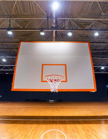A well-lit indoor basketball court featuring a vibrant hoop and polished wooden floor.の素材