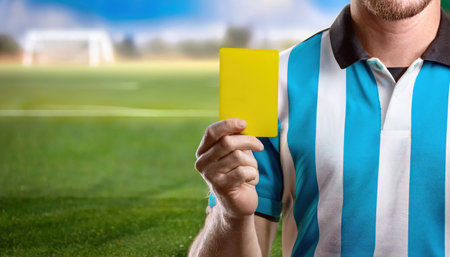 A referee displays a yellow card on the field as players await decisions in the game.の素材