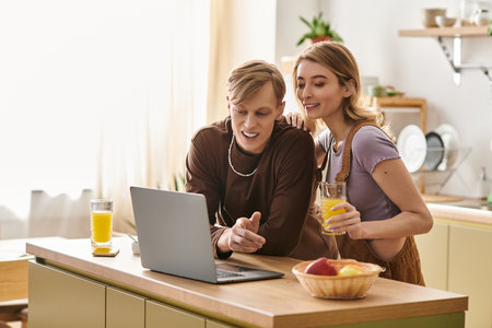 A happy couple enjoys drinks and laughter while discovering tasty recipes in their cozy kitchen.のeditorial素材