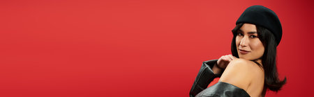 Confident young woman showcases a trendy outfit against a bright red backdrop.