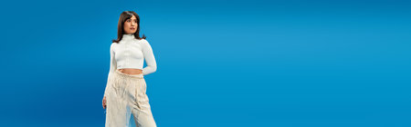 Young Asian woman confidently models trendy attire against a vibrant blue backdrop.