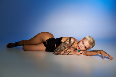 A stylish young woman with striking tattoos lies on the floor, highlighting her appeal.のeditorial素材