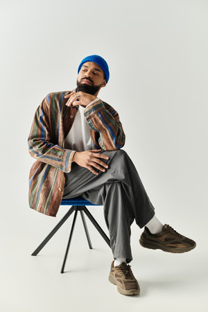 A fashionable young man with a beard sits elegantly on a modern chair, deep in thought.のeditorial素材