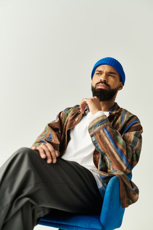 Young man with a fashionable ensemble thoughtfully poses while seated, showcasing modern style.のeditorial素材