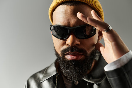 Handsome man sports sunglasses and a beanie while posing stylishly against a gray backdrop.