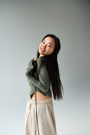 A young asian woman smiles while playfully showing off her chic outfit in a serene studio setting.の写真素材