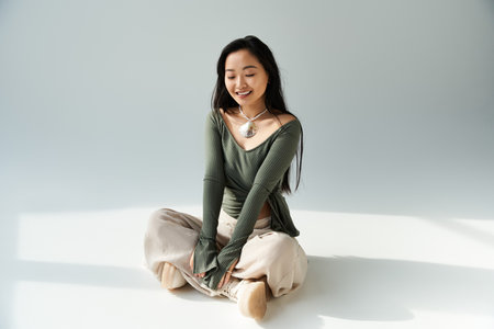 A young woman sits gracefully on the floor, radiating joy and style in a softly lit room.のeditorial素材