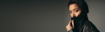 Young woman in trendy attire poses with confidence, showcasing her fashion sense in a sleek studio.の写真素材