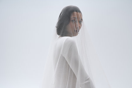 A beautiful young bride poses gracefully, adorned in her bridal veil, radiating joy and elegance.
