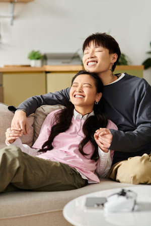 A young asian couple enjoys a cozy afternoon, laughing and bonding on a comfortable couch.の写真素材