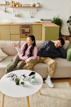A young Asian couple shares laughs and snacks on a cozy sofa in their modern home.の写真素材