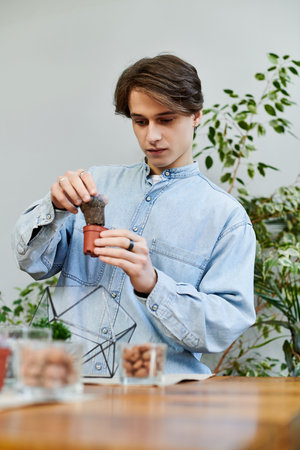 Young artist engages in planting activities while surrounded by lush greenery and art supplies.のeditorial素材