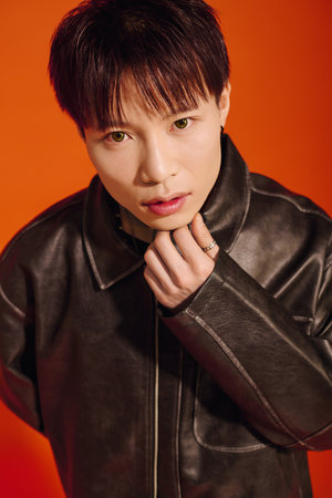 A young man in a bright orange setting displays his stylish outfit and captivating look.のeditorial素材