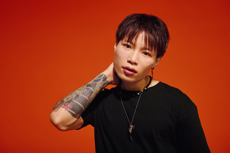 A charismatic young Asian man poses stylishly against a vibrant orange background.のeditorial素材