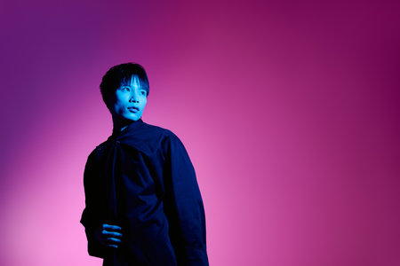 A stylish Asian man shines in colorful light, exuding charm and confidence.