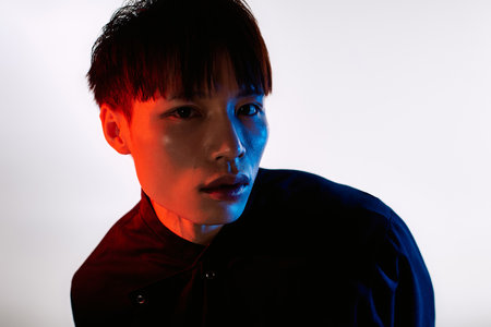 Charismatic young man showcases unique style with confident pose and striking colors in background.のeditorial素材