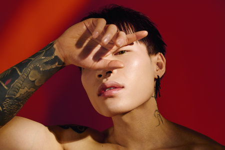 Handsome young man playfully shielding his eyes with a hand while showcasing his tattoos.