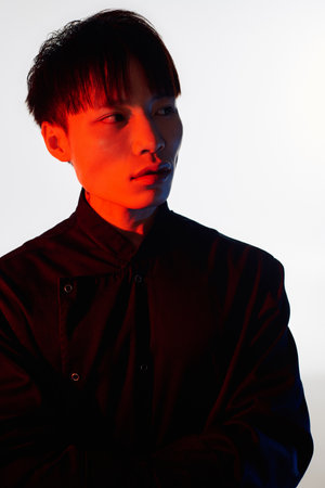A young Asian man poses confidently against a creatively lit, colorful backdrop.のeditorial素材