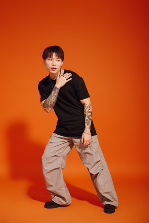 A handsome young man showcases his fashion sense in a playful pose against warm orange tones.のeditorial素材