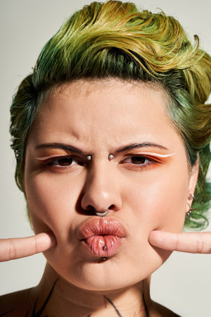 A confident young woman playfully poses, showcasing her artistic makeup and trendy hair.のeditorial素材