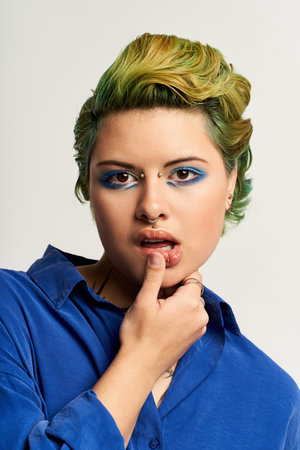 A young woman displays her stylish attire and vibrant hair with confident, expressive makeup.