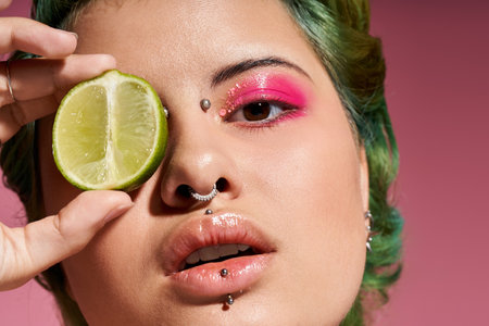 A young woman holds a lime to her eye, highlighting her bold makeup in a vibrant, colorful setting.のeditorial素材