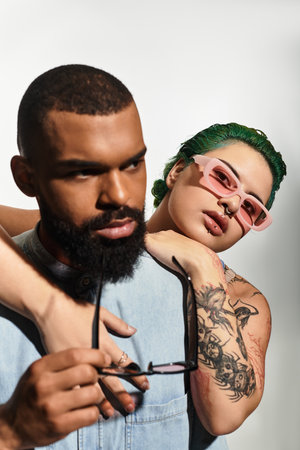 Multicultural young couple poses in vibrant outfits, showcasing stylish sunglasses in a studio.のeditorial素材