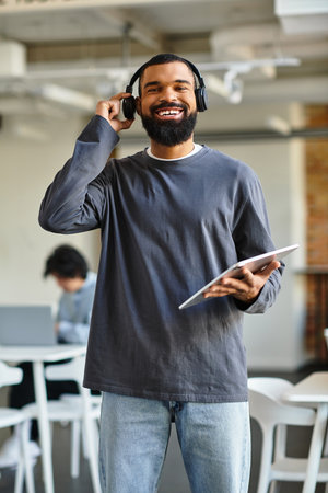 A man smiles with headphones and a tablet in a modern office during work hours.のeditorial素材