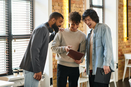 Three colleagues engage in cheerful discussion while reviewing a digital presentation togetherのeditorial素材
