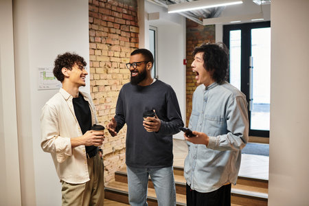 Three colleagues enjoy a lively discussion at work, sharing laughs and warm beverages together.