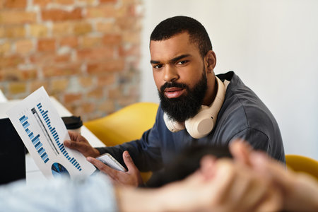 A man analyzes data reports while collaborating with a colleague in a modern office space.のeditorial素材