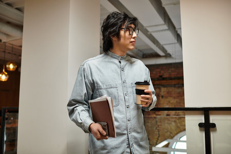 A focused person sips coffee in a stylish office, notebook in hand, deep in thought.