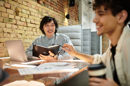 Two professionals share ideas and collaborate in a stylish office environment with warm lighting.のeditorial素材