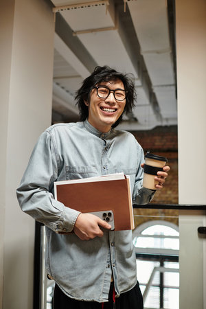 A glasses wearing person in casual attire enjoys coffee with notebooks in a vibrant workspace.のeditorial素材