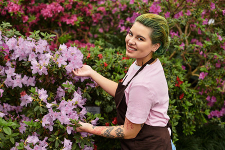 In a vibrant greenhouse, a young woman smiles while tending to beautiful blooming flowers.のeditorial素材