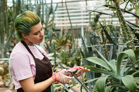 A young woman carefully prunes plants in a lively greenhouse filled with various greenery.のeditorial素材