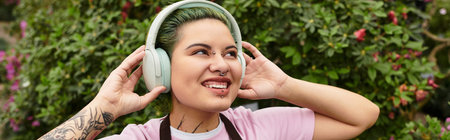 A young woman in a greenhouse listens to music with a joyful smile while caring for plants.のeditorial素材