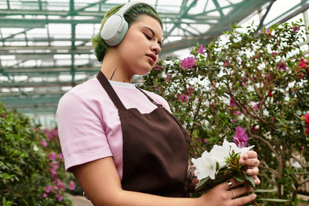Focused young woman carefully arranges beautiful white flowers in a vibrant greenhouse environment.のeditorial素材