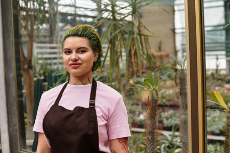 A young woman with green hair tends to plants in a bright green house, enjoying her work.のeditorial素材