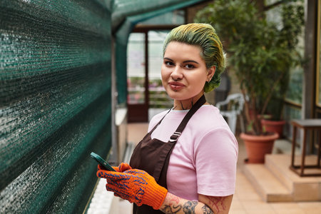 Engaged in gardening, a young woman with green hair enjoys her work in a bright greenhouse.のeditorial素材
