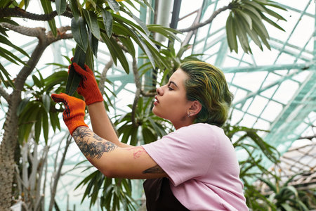 Passionate young woman cares for thriving plants in a lush greenhouse filled with greeneryのeditorial素材