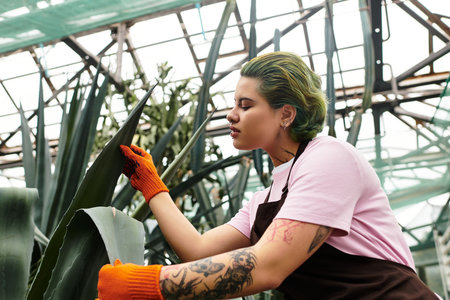 Young woman nurturing plants in a sunlit greenhouse, surrounded by lush greenery.のeditorial素材